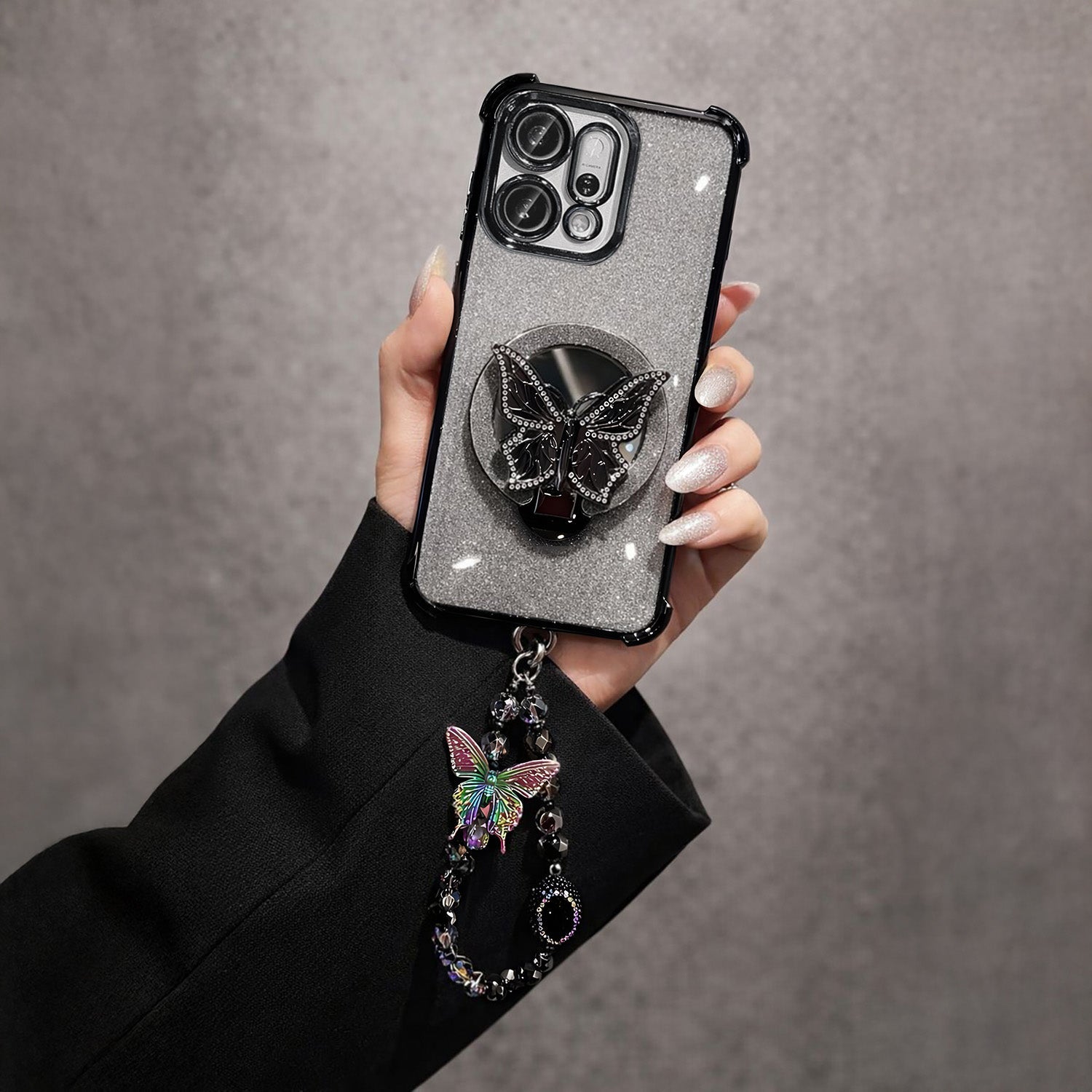 Oppo Reno 14 5G Hand holding a phone case with a butterfly design and charm on a gray background